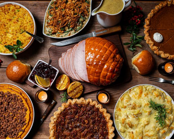 Thanksgiving dinner spread on a table featuring a ham, several pies, and sides Credit: Jed Owen